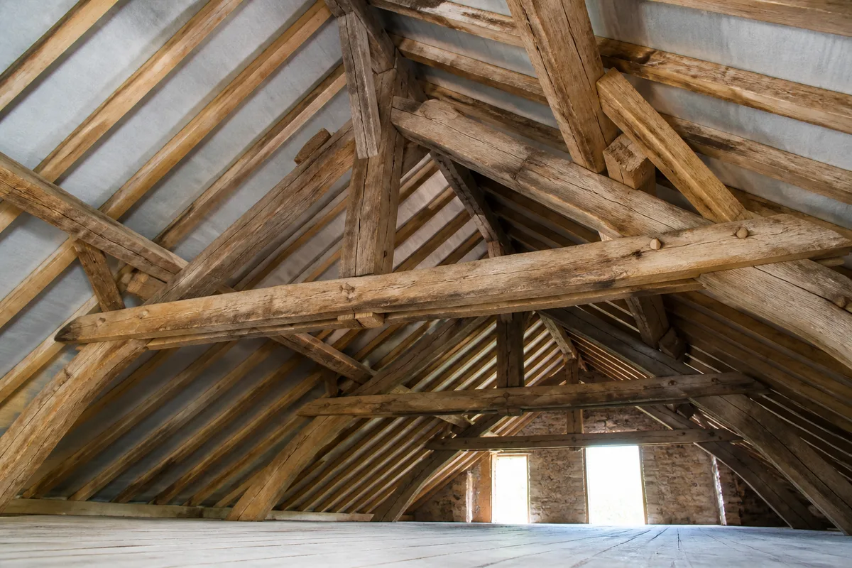 Charpente traditionnelle en bois vue depuis le sol d&rsquo;un comble vide et poussiéreux