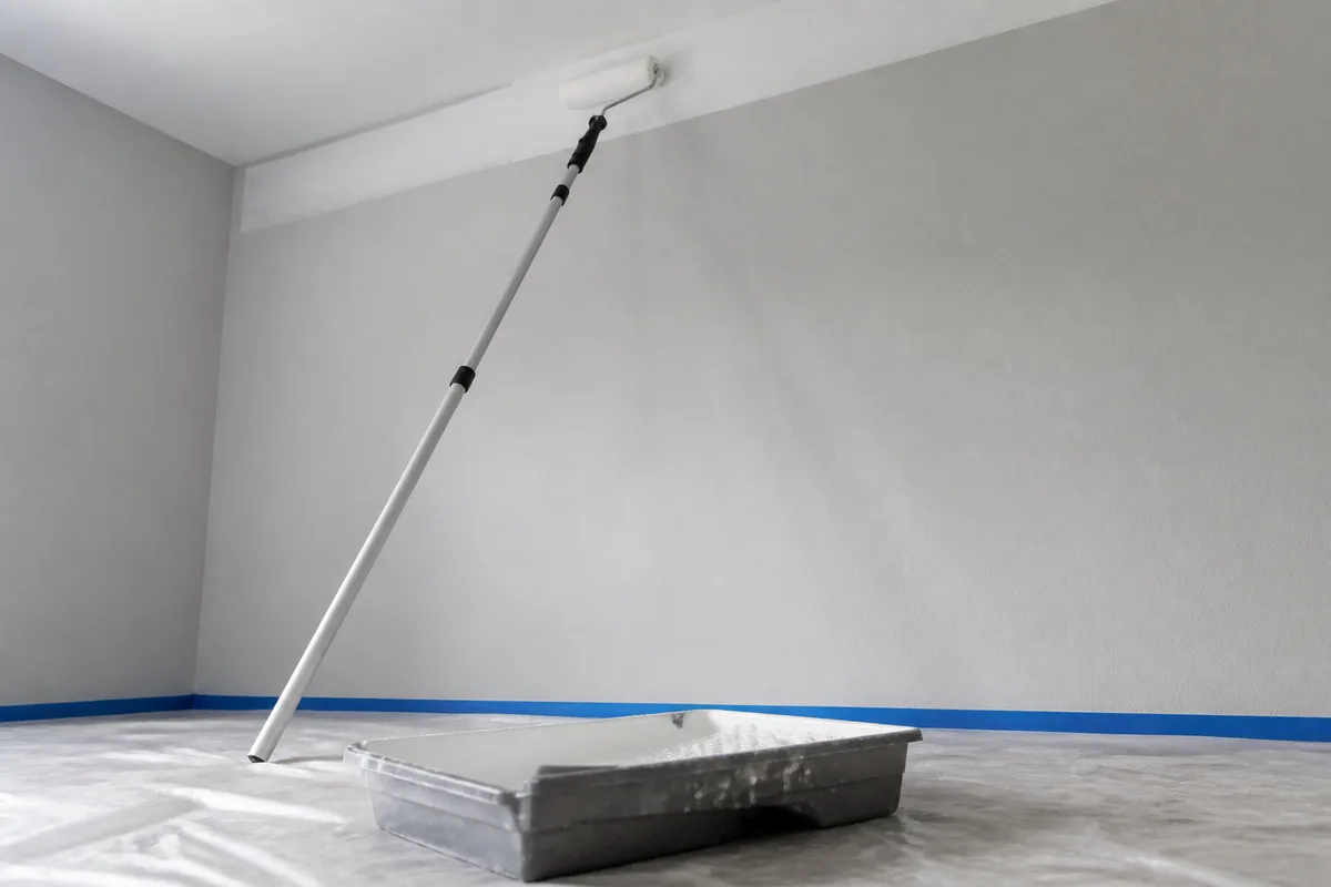 Rouleau anti-goutte monté sur perche télescopique appliquant la peinture sur un plafond blanc