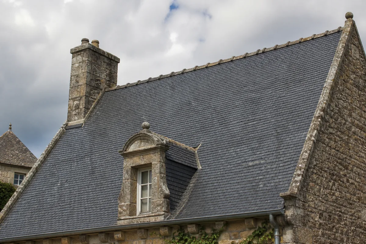 Toiture en ardoises à forte pente sur une maison ancienne en pierre